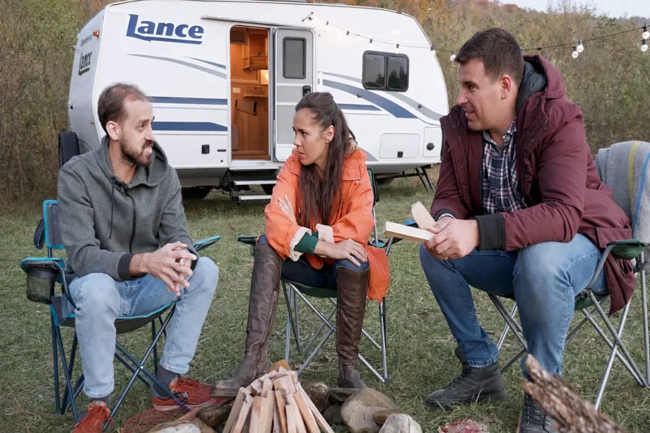 Friends sitting around a campfire beside a Lance travel trailer during a cozy outdoor camping trip.
